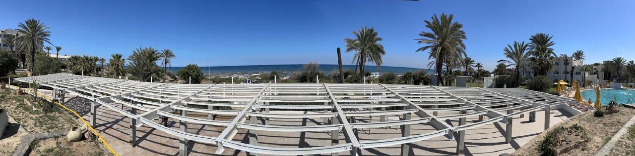 POLYENCO - Ombrière métallique en bord de mer, structure cintrée avant couverture